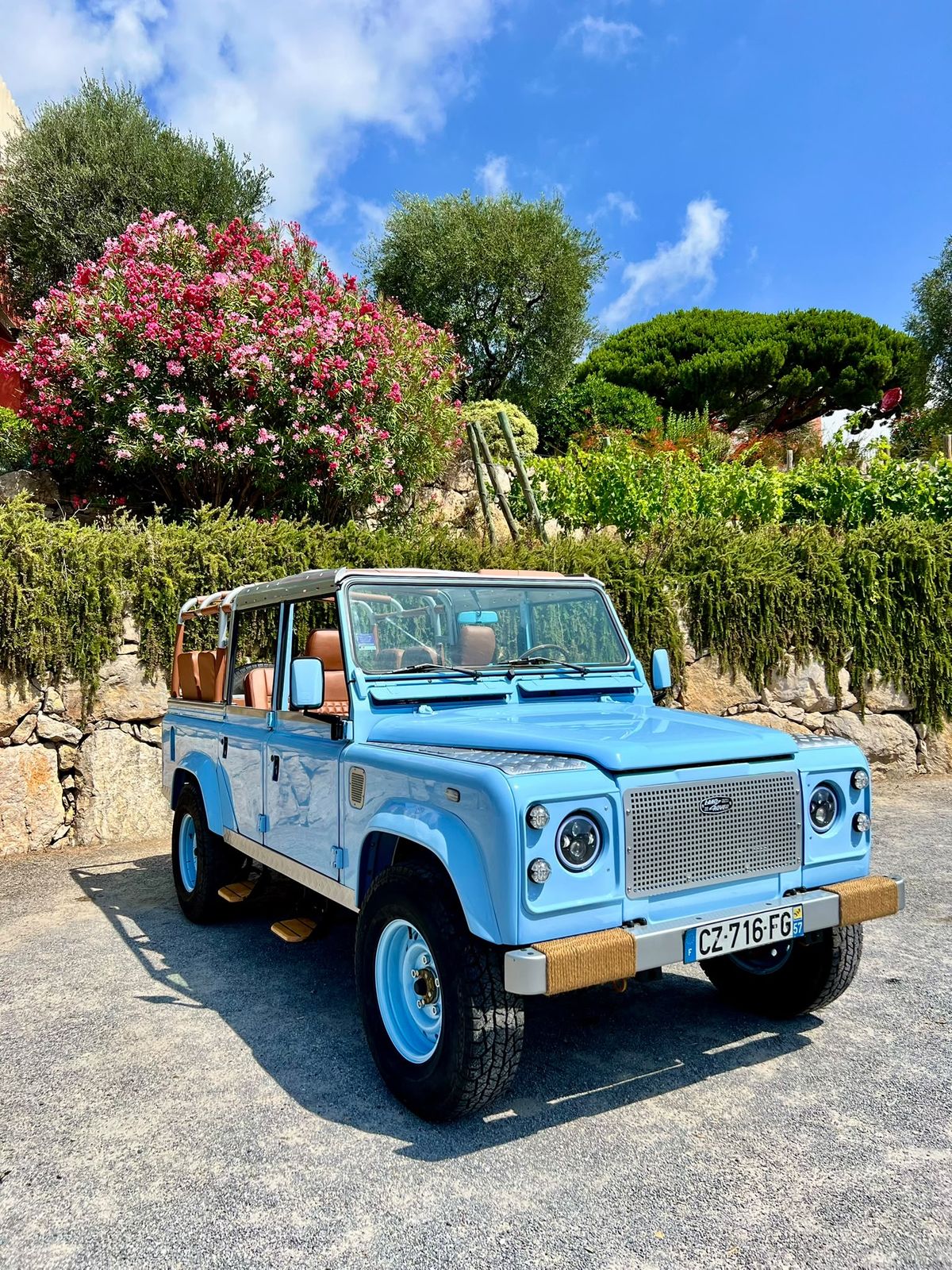 Land Rover Defender bleu ciel garé devant des vignes en fleurs