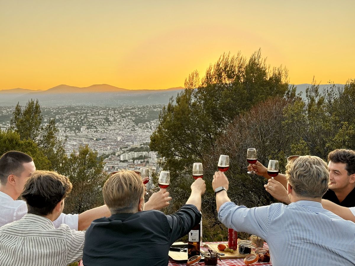 Toast au coucher du soleil sur les hauteurs de Nice, verres de vin levés face à la Baie des Anges